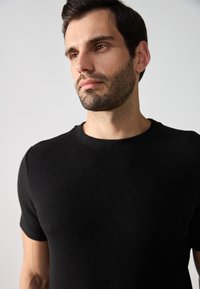 Maglione a maniche corte nero a coste con scollatura a girocollo, caratterizzato da un tessuto testurizzato che mette in risalto la struttura e la vestibilità del capo.