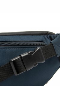 Marsupio in nylon blu con una cintura nera e testurizzata, dotato di chiusura con zip e hardware a fibbia, che presenta un design essenziale.