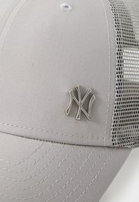Grå baseballcap med mesh bag. Har et sølvlogo og detaljeret syning langs skyggen. Tekstureret stof med struktureret design.