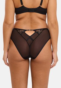 Culotte en dentelle noire et en mesh avec un design à taille haute, des détails entrecroisés, un matériau transparent et un dos ouvert. Texture lisse.