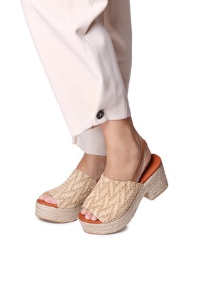 Sandali intrecciati beige con parte superiore testurizzata, punta aperta e tacco grosso. Accentuati con una soletta marrone e una fascia trasparente sul tacco.
