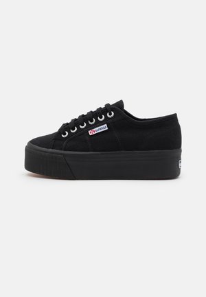 Black canvas sneakers with a platform sole, featuring silver eyelets, flat laces, and a small logo tab on the side for branding.