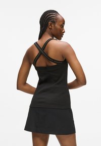 Must särg ilma varrukateta, millel on ristiülesed rihmad, ribatakstega tekstuur ja metallikaktsendid rihmade äärel. Kanda musta seeliku koos.