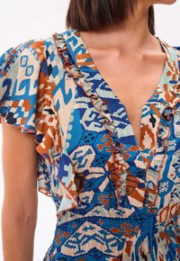 Monivärinen mekko, jossa on sininen, oranssi ja vaaleanbeige abstrakti kuvio. V-neck-malli, jossa on volangit ja teksturoitu kangas.