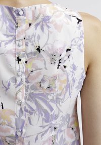 Ärmlös blus i lätt material med ett blommönster i pastellfärger, med knäppning bak och en slät yta.