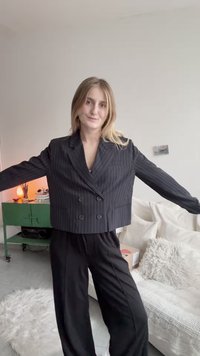 Mustritud must cropped bleiser kahekordse nööpimisega ja sisselõigatud kraega, millele on juurde pandud laiad mustad püksid. Modell poseerib käed välja sirutatud.