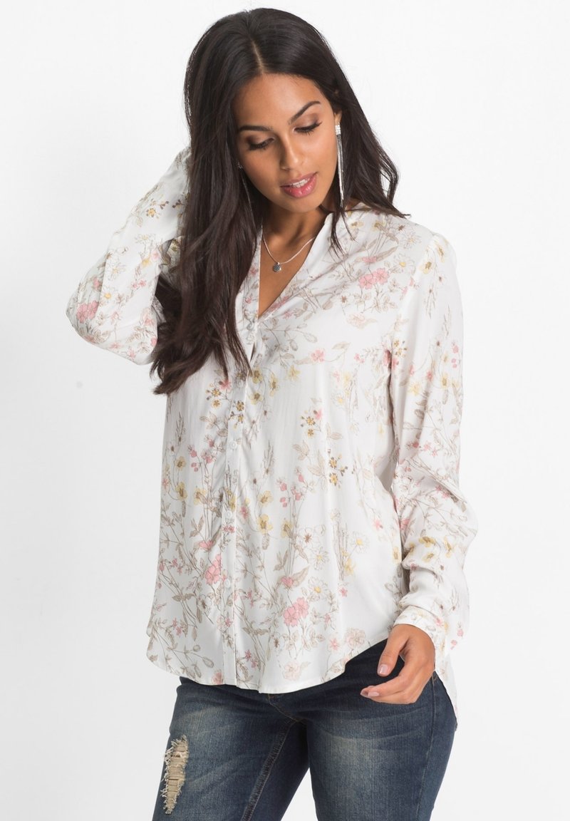 Camicia bianca con bottoni, decorata con un motivo floreale nei toni del rosa e del giallo, realizzata in tessuto leggero. Maniche lunghe con orlo curvato.