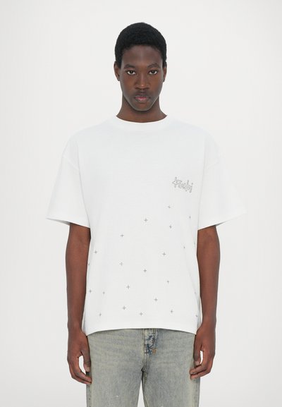 Witte katoenen t-shirt met korte mouwen, voorzien van verspreide grijze plustekens en een klein geborduurd logo op de borst.