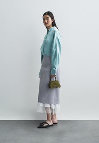 Ανοικτό μπλέ πουκάμισο με μακριά μανίκια, γκρι φούστα με δαντελένια λεπτομέρεια, μαύρες επίπεδες γόβες και μια μικρή ελιά ολόκληρη τσάντα. Λείες υφές και απλές γραμμές.