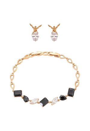 Złota bransoletka z naprzemiennie ułożonymi czarnymi i przezroczystymi kamieniami szlachetnymi oraz złote kolczyki w kształcie wróżek trzymające przezroczyste owalne kamienie na białym tle.