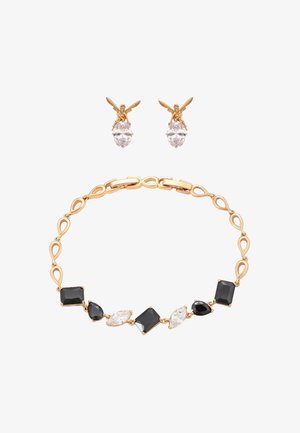 Złota bransoletka z naprzemiennie ułożonymi czarnymi i przezroczystymi kamieniami szlachetnymi oraz złote kolczyki w kształcie wróżek trzymające przezroczyste owalne kamienie na białym tle.