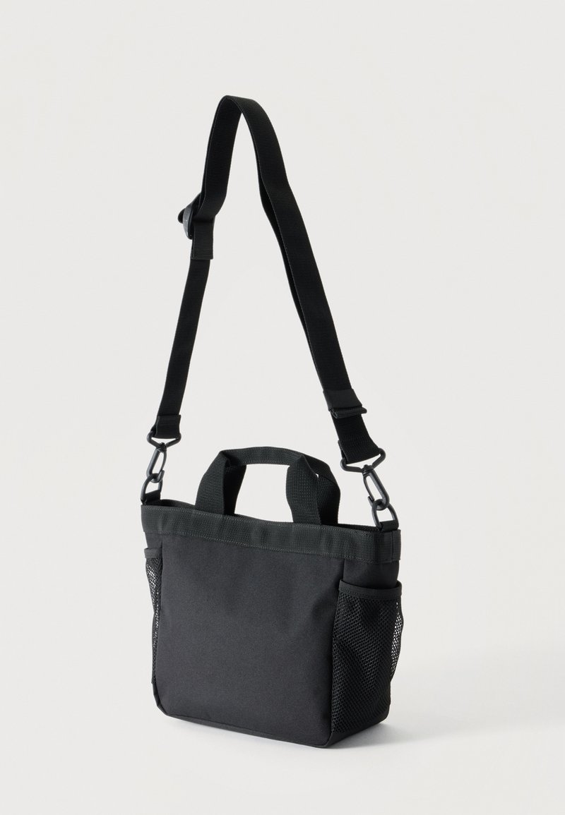 Piccola borsa a tracolla in tessuto nero con tracolla regolabile, due manici corti e tasche laterali in mesh su sfondo bianco.
