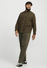 Olive green button-up shirt with a pocket, paired with olive pants and black sneakers. Fabric appears soft; shirt has a relaxed fit.