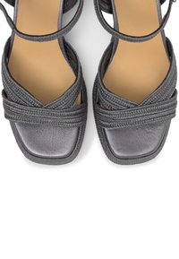 Sandales noires à brides avec des lanières en cuir tressé et un bout carré sur une semelle beige.