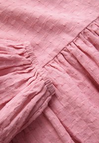 Tessuto rosa chiaro strutturato con motivo a griglia e dettagli arricciati, che mostrano particolari morbidi e leggermente stropicciati.