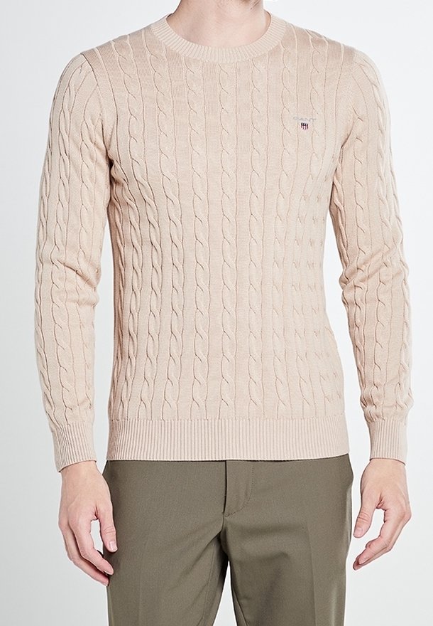Beiger Kabelstrickpullover mit langen Ärmeln und gerippten Bündchen und Saum. Mit kleinem Logo auf der Brust. Weicher Stoff und figurnaher Schnitt.