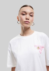 Hvid bomuld T-shirt med et pink grafisk print af en jordbærcocktail på venstre brystområde, med korte ærmer og en afslappet pasform.