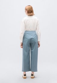 Lichtblauwe wijde broek met hoge taille, gemaakt van een gladde stof. Gecombineerd met een wit shirt met lange mouwen en casual schoeisel.