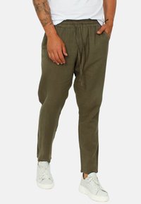 Pantaloni in misto lino verde oliva con vita elastica, cordino regolabile, tasche laterali e design a gamba affusolata. Indossati con sneakers bianche.