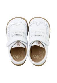 Zapatos de niño pequeños, blancos con suelas marrones, perforaciones decorativas, cordones y tiras de velcro, vistos desde arriba sobre un fondo blanco.