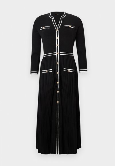 Robe/cardigan en tricot noir avec une texture côtelée, manches longues, détails en accent blanc, poches avant et boutons dorés le long de la fermeture.