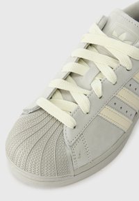 Szare sneakersy z fakturowanym gumowym noskiem, białymi akcentami i beżowymi paskami. Posiadają płaskie białe sznurowadła oraz gładką zamszową cholewkę.