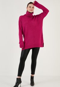 Fuksia suuruse soe kampsun kõrge kaelusega, soonikkoes varrukate ja äärega, koos mustade leggins'ite ja läikivate pahkluusaabastega.