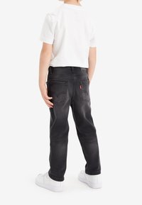 Svarta denimjeans med rak skärning, bakfickor och röd Levi's-logotyp. Matchas med en vit T-shirt och vita sneakers.