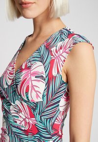 Blomsterkjole med et levende design af pink og grønne tropiske blade, stoffet har en glat tekstur, og en tætsiddende v-hals.