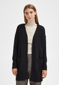 Cardigan noir en tricot avec un col en V, ouvert à l'avant et deux poches à l'avant. Doté de manches longues et d'une texture douce.