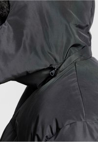 Sort pufferjakke med tekstureret overflade, med hætte, lynlåslukning og justerbare siden straps. Detaljeorienteret design.