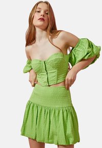 Conjunto de dos piezas verde y texturizado que presenta una parte superior ajustada, sin tirantes, con detalles de botones y una falda mini acampanada con acentos fruncidos.