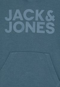 Džemper s kapuljačom u tamno tirkiznoj boji, s prednjim džepom i velikim bijelim natpisom "JACK & JONES" otisnutim na prsima.