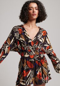 Camisa de manga larga con estampado floral, escote en v y cintura elástica. Fondo oscuro con acentos en rojo, azul y crema; tela ligera.