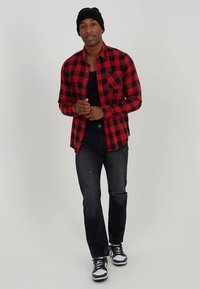 Καρό φανέλα φανέλας κόκκινου και μαύρου χρώματος, μαύρο τοπ χωρίς μανίκια, ξεφτισμένο μαύρο τζιν και μαύρα αθλητικά παπούτσια με λευκές λεπτομέρειες. Απλό πλεκτό σκουφί.