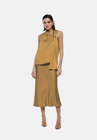 Una blusa senza maniche di colore giallo senape con un design drappeggiato e un accento dorato, abbinata a una gonna fitted coordinata. Texture liscia.