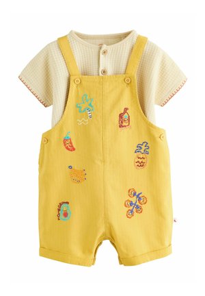 Yellow baby romper with embroidered tropical motifs worn over beige short-sleeve, buttoned textured shirt.