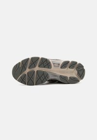 Semelle de chaussure de sport pour homme, avec une surface en caoutchouc noir texturé, un design courbé et des accents gris clair, offrant traction et soutien.