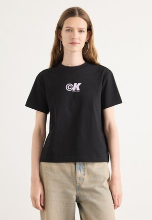 Zwarte katoenen t-shirt met een ronde hals en korte mouwen. Bevat een roze logo op de borst. Gekoesterd met lichtblauwe jeans.
