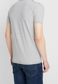 Grijs en witte gestreepte t-shirt met korte mouwen, ronde hals en een zachte textuur, gedragen met blauwe denim jeans.