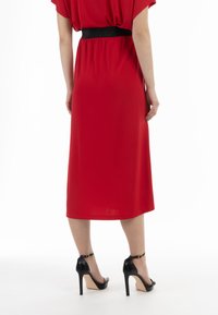 Rode midi-jurk met korte mouwen, elastische zwarte tailleband en een gladde textuur, gecombineerd met zwarte hoge hakken.