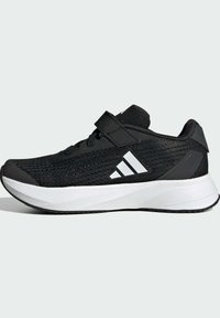 Zapatilla deportiva negra con parte superior de malla, correa de Velcro, acentos blancos y suela texturizada. Cuenta con una entresuela acolchada para mayor soporte.