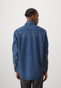 Camicia in denim, blu scuro, con un taglio classico, colletto a punta, maniche lunghe e polsini con bottoni. Presenta un orlo curvo e un tessuto testurizzato.