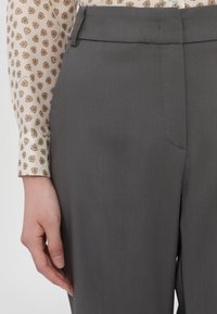 Gray tailored trousers featuring a flat front, subtle texture, and a side pocket. The hand shown rests lightly against the fabric.