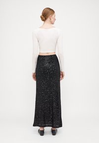Witte langemouwen crop top gecombineerd met een zwarte, pailletten maxi rokje. De rok heeft een slim fit en een vloeiende stijl. Zwarte schoenen maken de look compleet.