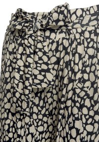 Svarta och beige abstrakta prickiga byxor med ett tygbälte knutet i en rosett i midjan.