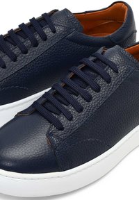 Granatowe skórzane sneakersy z teksturowanym wykończeniem, płaskimi sznurówkami i kontrastowym pomarańczowym wykończeniem wewnętrznym. Charakteryzują się białą gumową podeszwą i subtelnymi detalami w postaci stężeń.