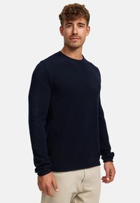 Dunkelblaues Langarmpullover aus texturiertem Stoff mit rundem Ausschnitt, der einen körpernahen Schnitt und taillierte Ärmel hat.