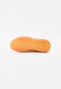 Orange rubber shoe sole with textured patterns, circular indentations, and smooth sections; features raised branding detail.