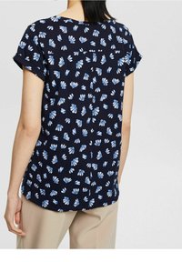 Granatowa bluzka z krótkim rękawem w biało-niebieski kwiatowy wzór, z zaokrąglonym dołem i detalem na plecach, wykonana z lekkiego materiału.